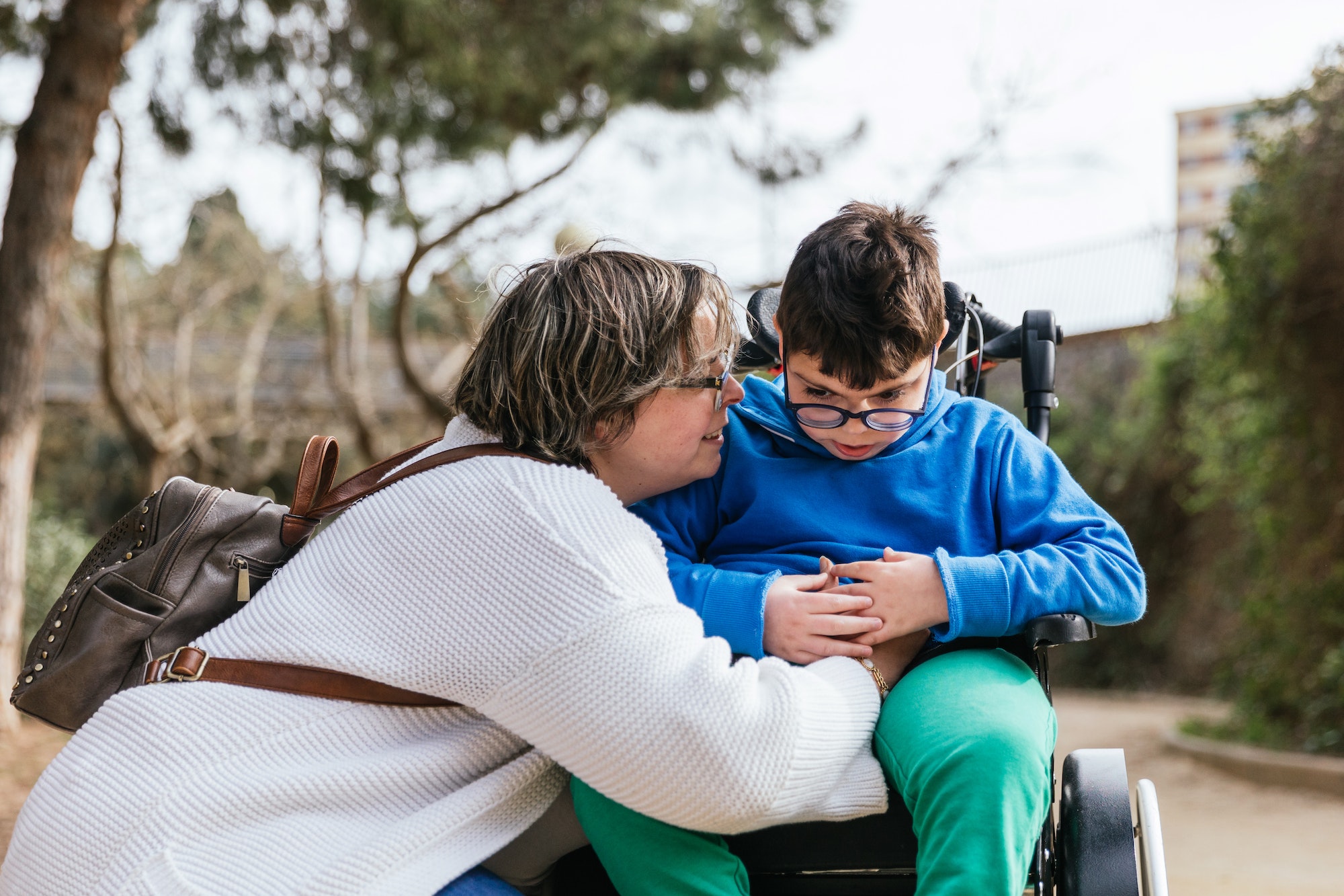 A loving mother hugging her son with a disability in a wheelchair in the park.